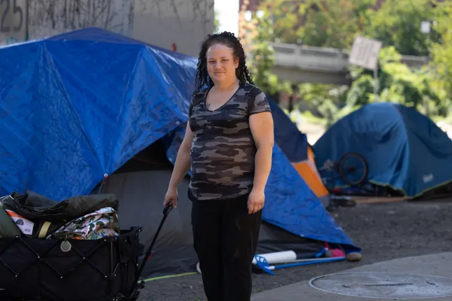 A woman stands outside to a wagon and a tent