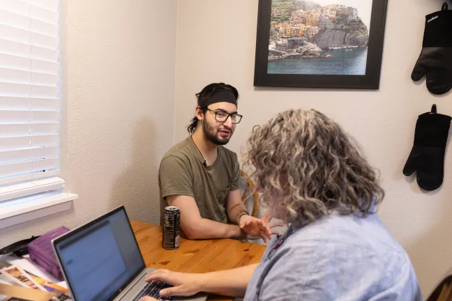 Jayson sits at a wooden table across a woman, Sarah Weller of Relay Resources, who is using a laptop.