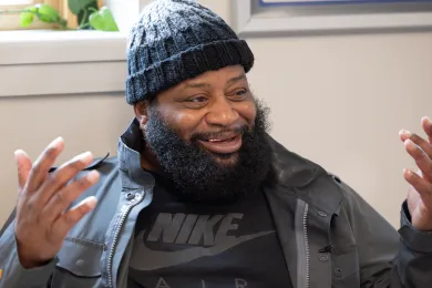 close up of a smiling man wearing a black beanie, black jacket and black shirt
