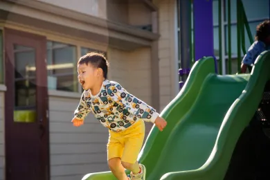 young kid jumping off of slide with a big smile