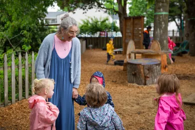 Children gathered around a teacher smiling in the playground